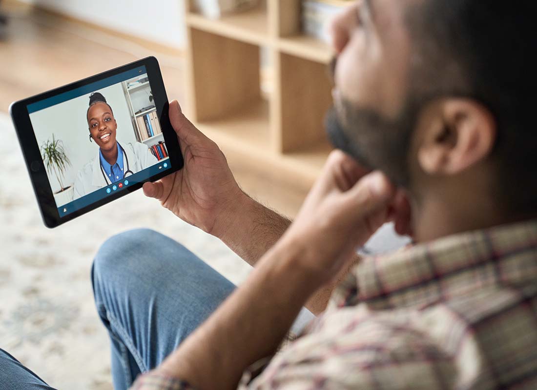 Group Telemedicine - Young Man Having an Online Virtual Telemedicine Video Call at Home with His Primary Care Physician Using a Tablet and Pointing to His Throat