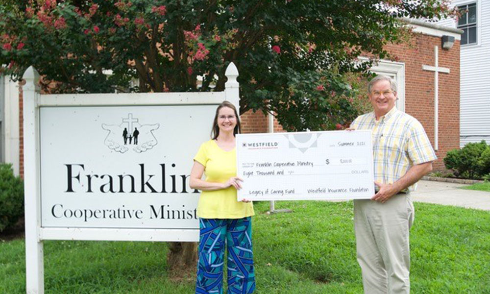 Manry Rawls Lends a Hand to Franklin Cooperative Ministries With $8,000 Donation - Man and Women Hold Up a Large Check Donation in Front of a Church